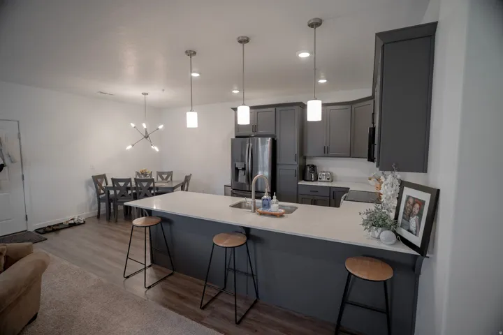 Open-concept living area with wood-finish flooring, a kitchen island with seating, dark shaker-style cabinetry, and recessed lighting