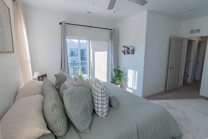 Sliding glass door leading to a balcony, ceiling fan, neutral wall paint, gray carpeting, and white trim throughout