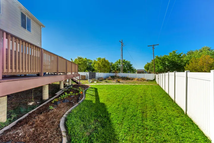 Elevated wood deck with railings, manicured lawn, white privacy fencing, and a mulched garden bed