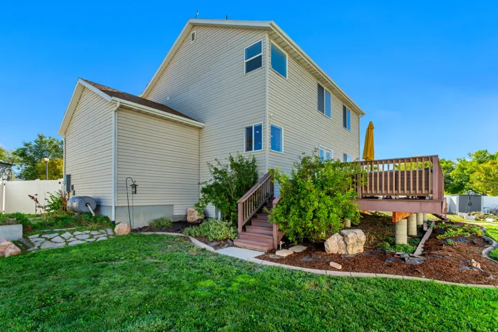 Elevated deck with wood railing and stairs, surrounded by landscaped garden beds, a stone pathway, and a vinyl privacy fence