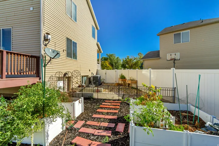 Multi-level backyard featuring a wood deck, raised garden beds, brick paver pathway, and a privacy fence