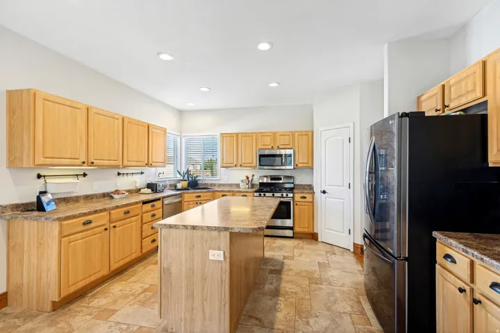 Kitchen featuring wood-finish cabinetry, stone-finish countertops, stainless steel appliances, a center island, and recessed lighting