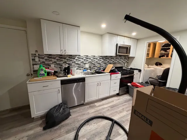 ADU Kitchen featuring white shaker cabinetry, stainless steel dishwasher, stainless steel microwave, gas range, and mosaic tile backsplash.
