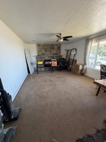 Stone-clad fireplace with a mantle, ceiling fan with integrated lighting, and wall-to-wall carpeting