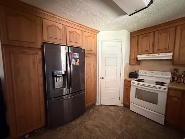 Warm wood-finish cabinetry, stainless steel refrigerator, white electric range with hood, and tile flooring