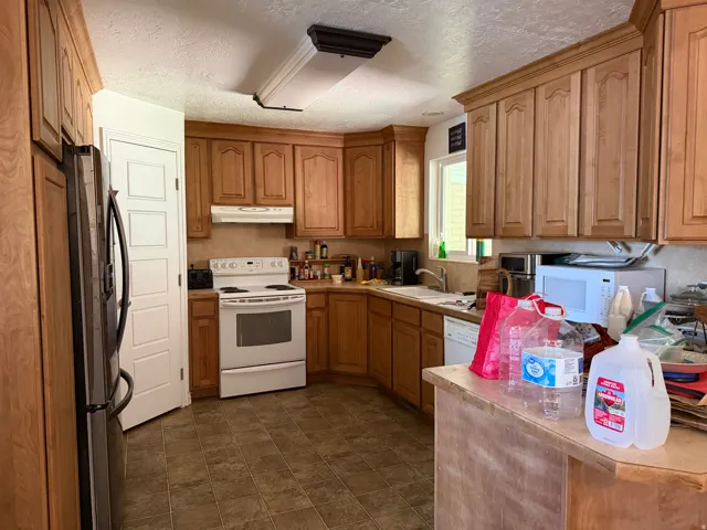 Kitchen featuring wood cabinetry, solid surface countertops, tile flooring, and white appliances