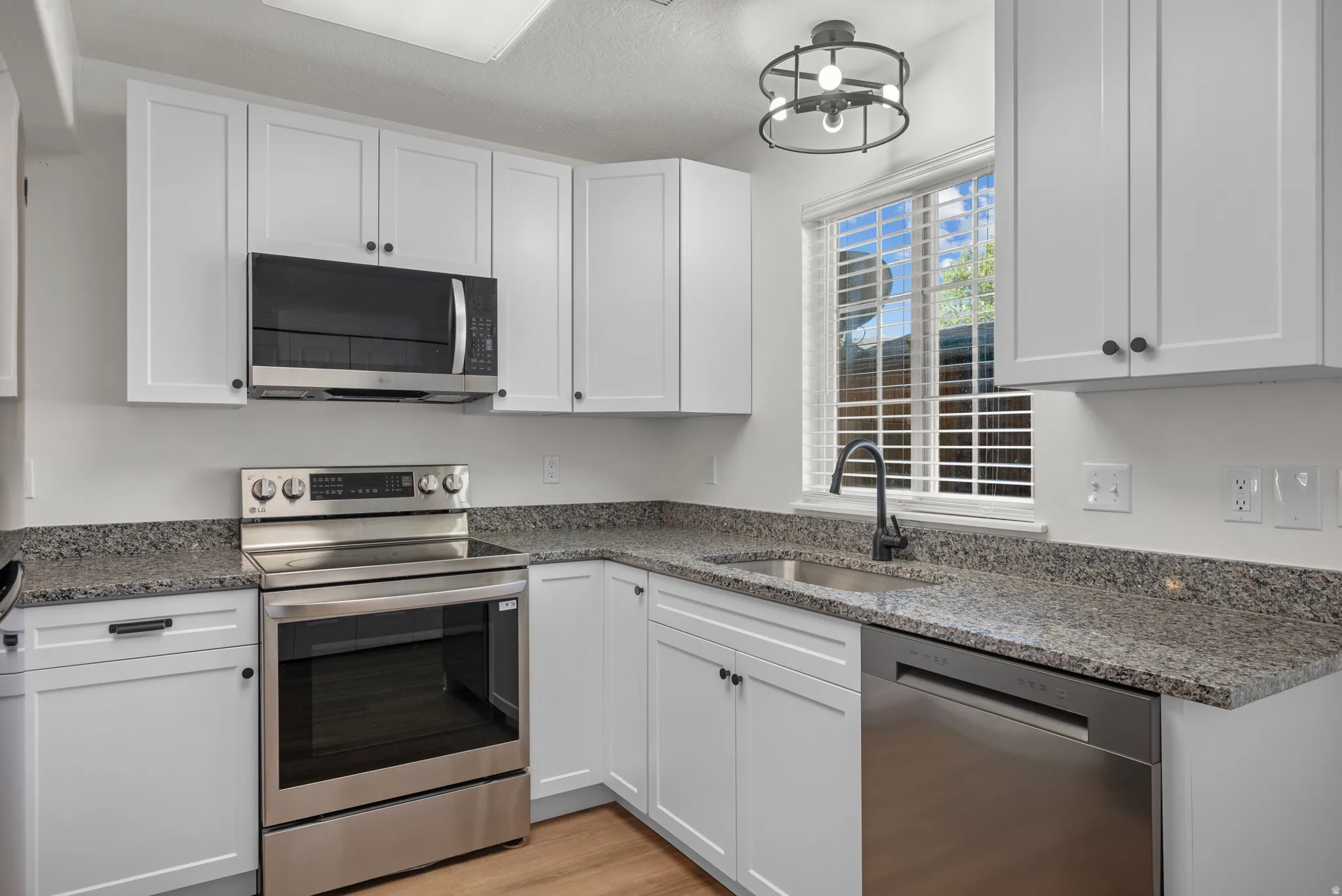 Kitchen featuring white cabinetry, stone-finish countertops, stainless steel appliances, and a window with blinds
