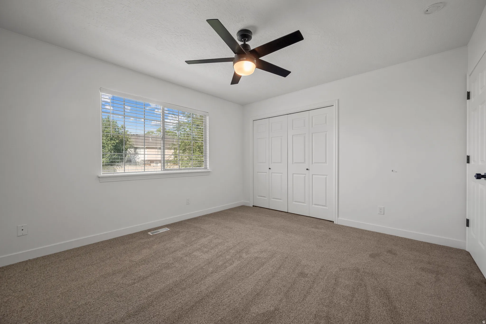 Neutral tone interior with carpet flooring, a window featuring horizontal blinds, and a ceiling fan with integrated lighting