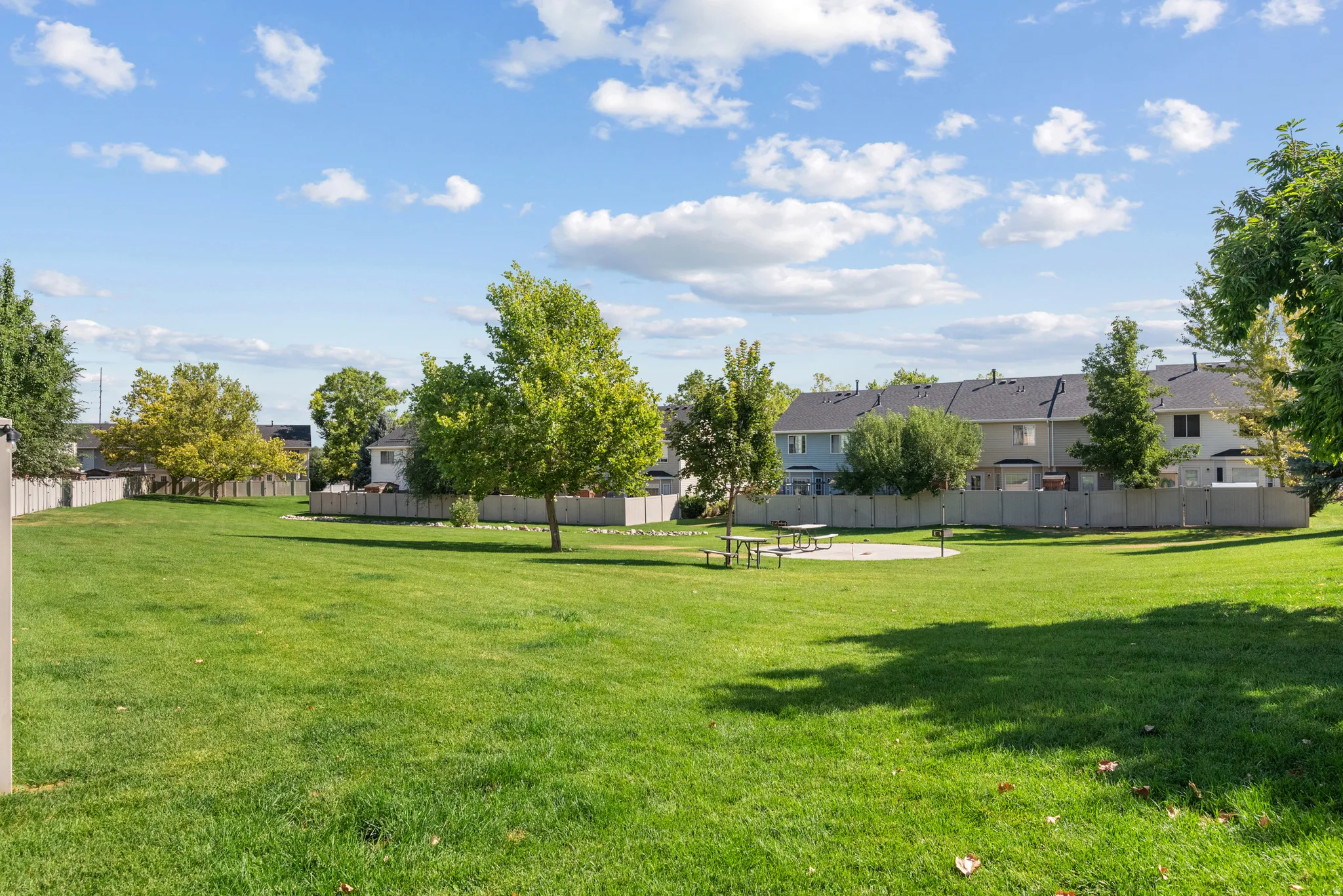 Expansive green space featuring mature trees, a picnic area, and perimeter fencing