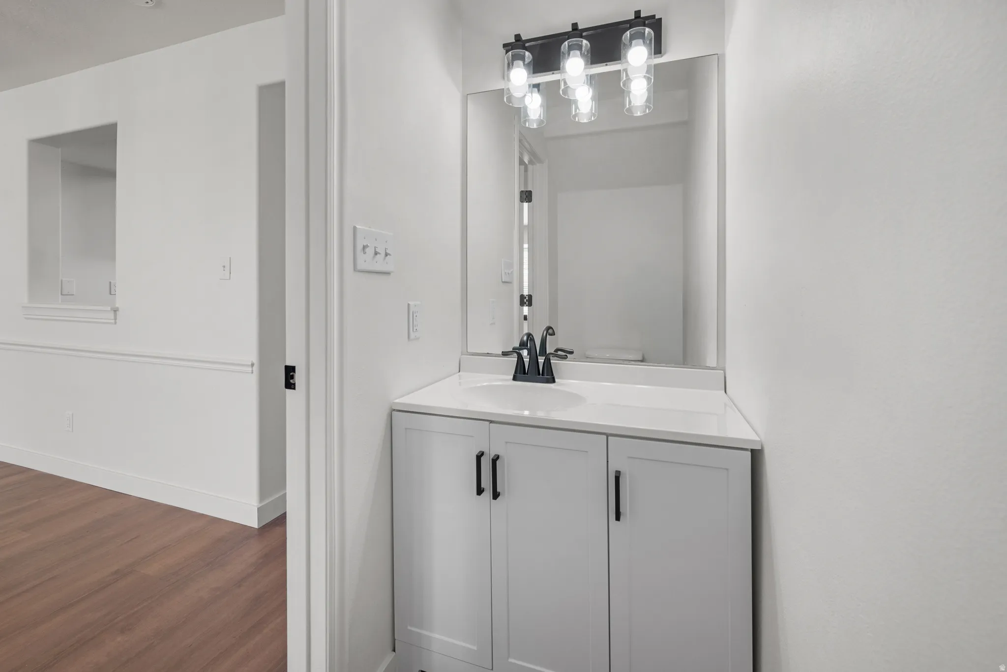 White vanity with shaker-style cabinet doors, a white countertop, and a black faucet
