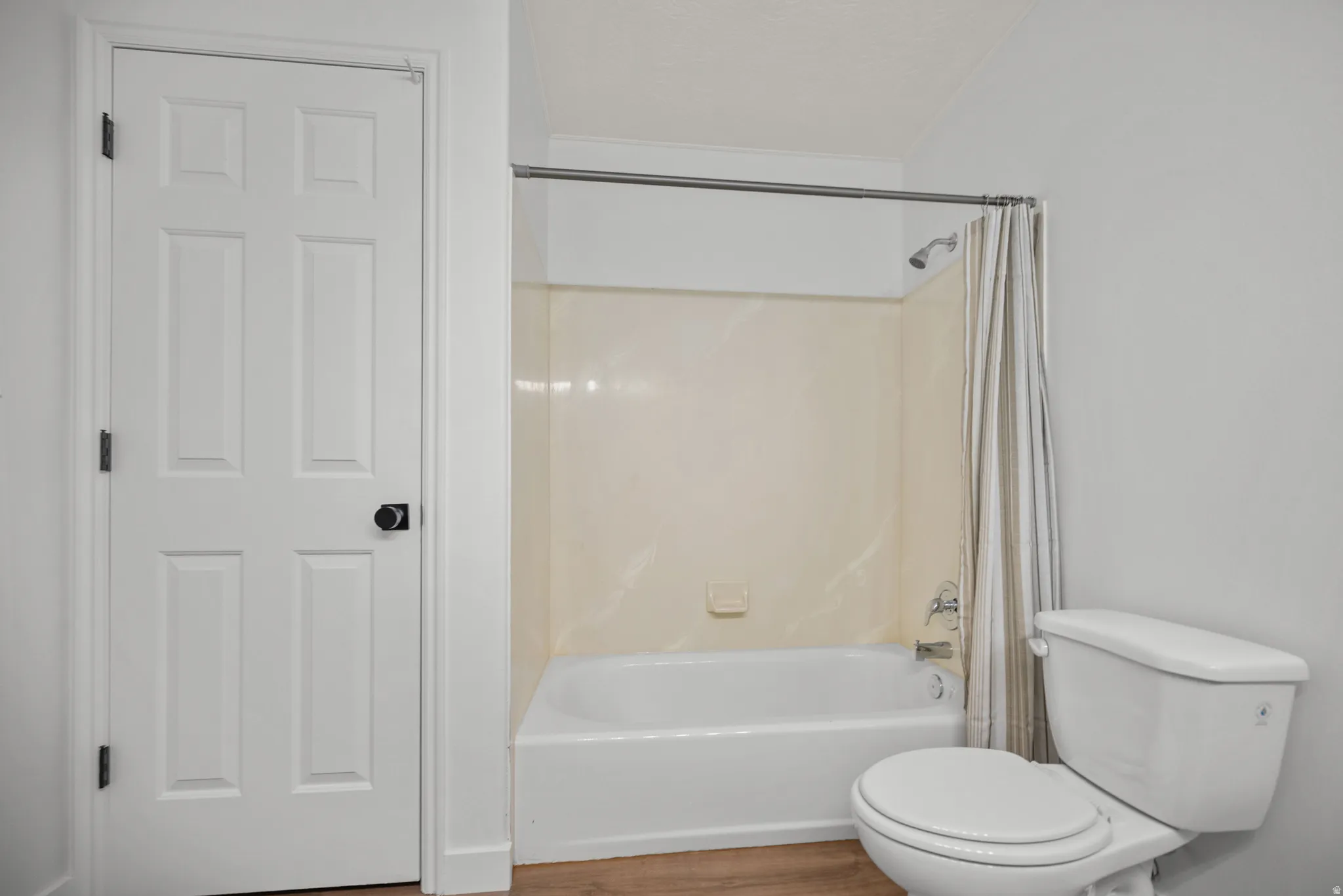 White paneled door with black hardware, white toilet, white bathtub, and wood-finish flooring
