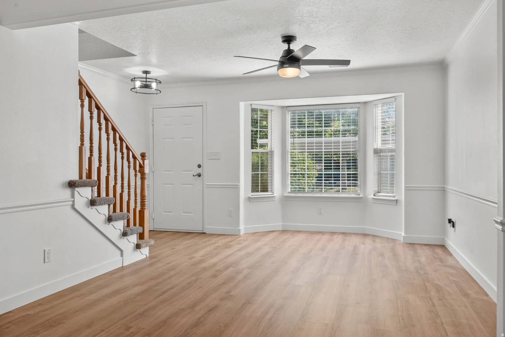 Open concept living area featuring wood-finish flooring, a bay window, and a ceiling fan with integrated lighting