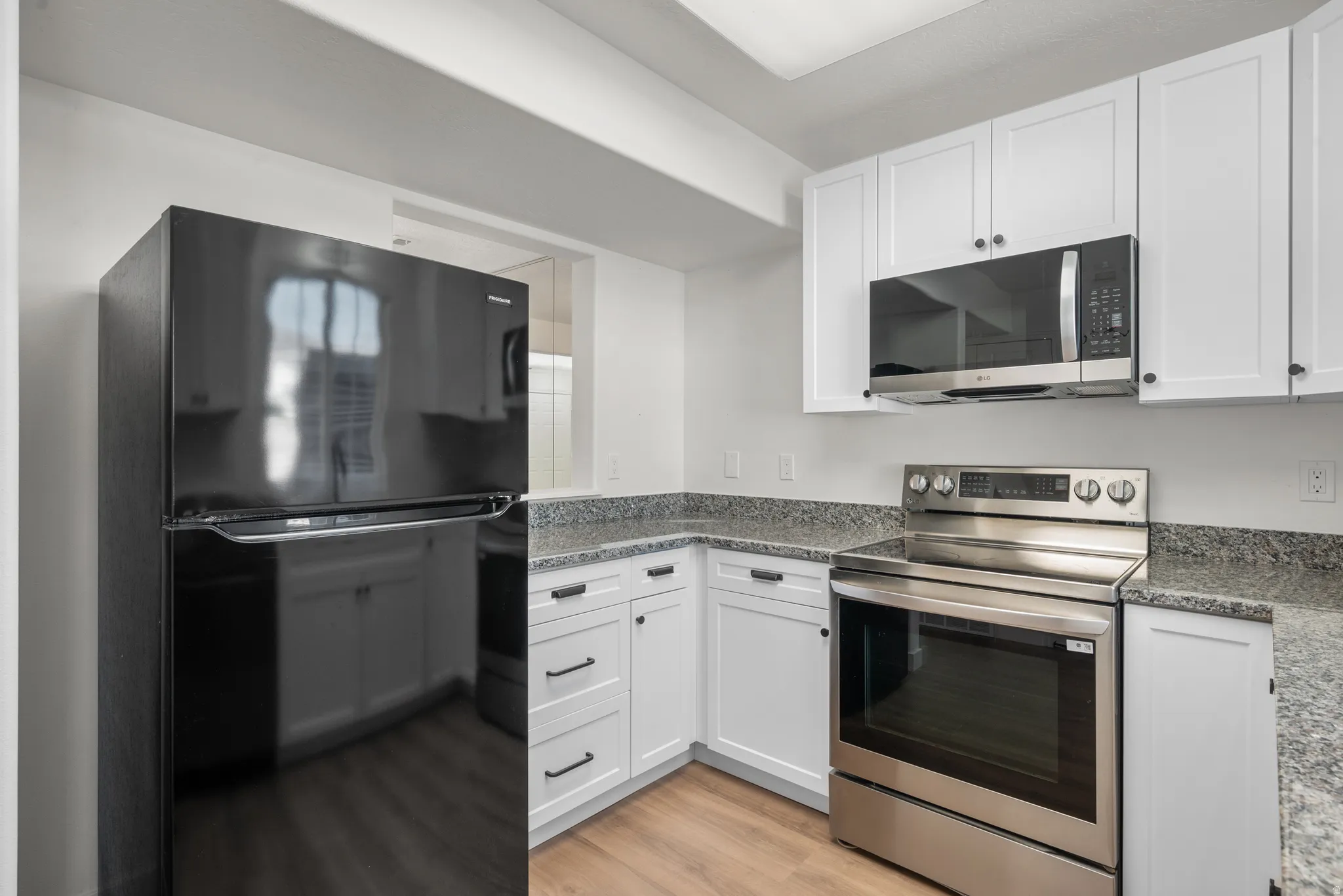 White shaker-style cabinetry, dark speckled countertops, stainless steel electric range, stainless steel microwave, and wood-finish flooring