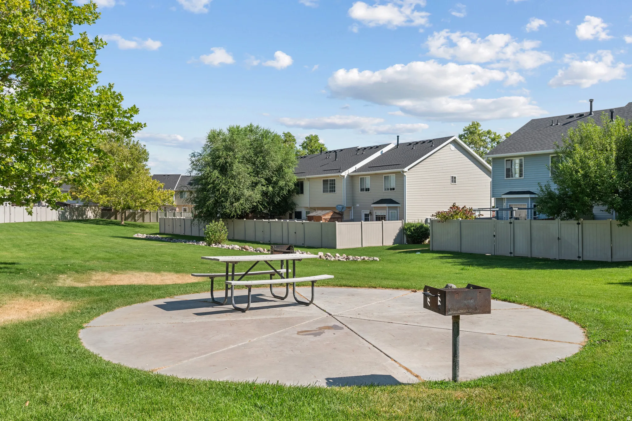 Expansive green space featuring a concrete patio, picnic table, and built-in grill