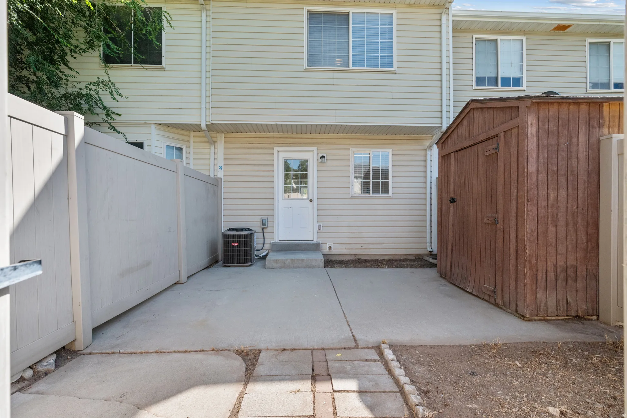 Paved patio area with a wooden storage shed, light-colored privacy fencing, and vinyl siding exterior