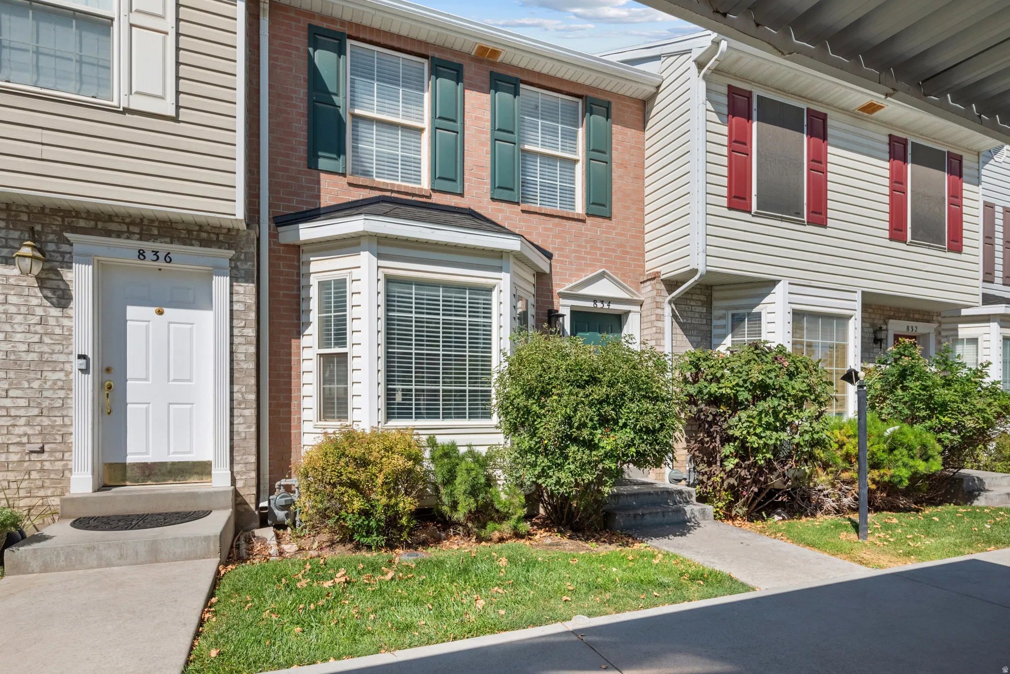 Brick and siding exterior featuring green window shutters, a bay window, and mature landscaping