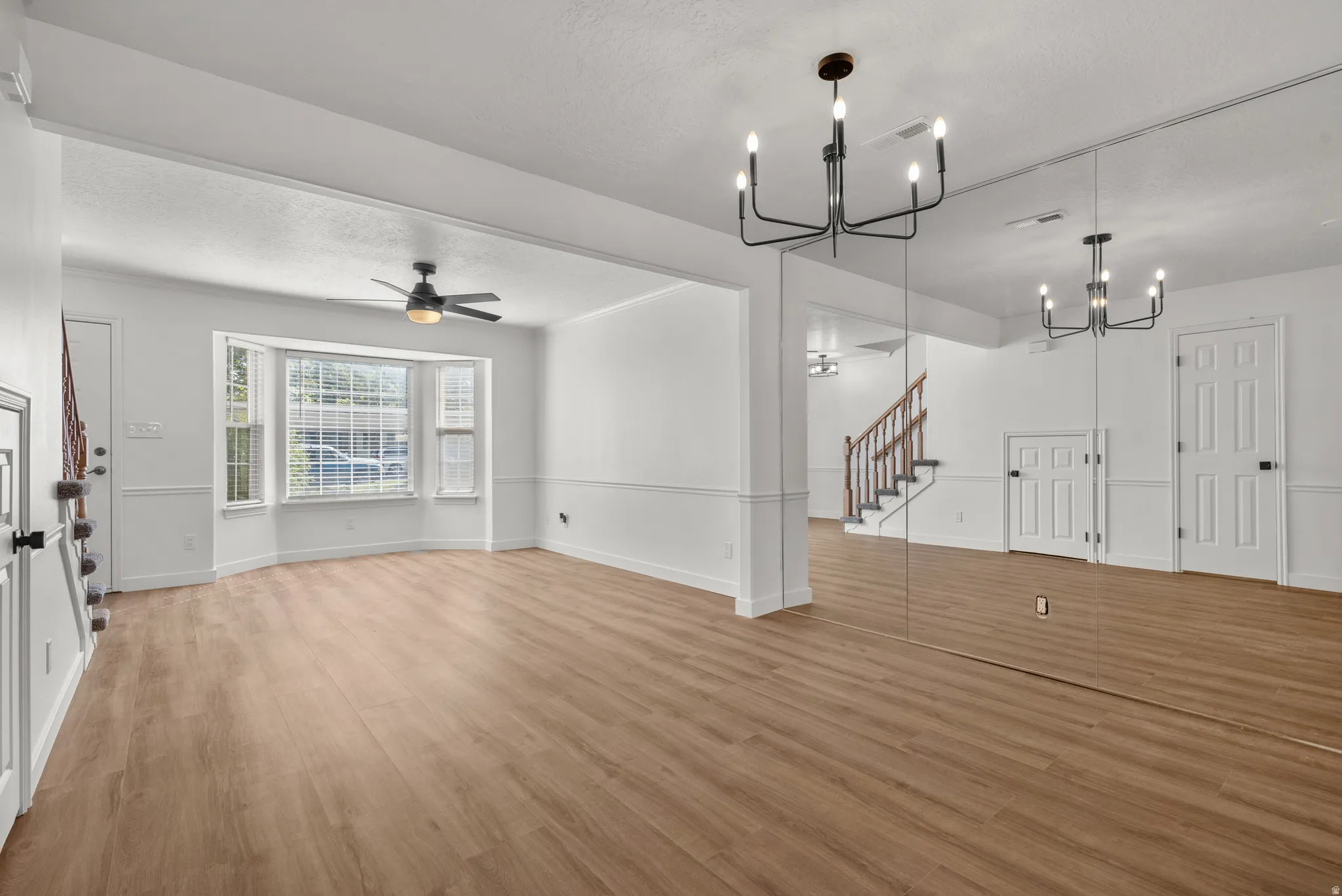 Recessed bay window, wood-finish flooring, staircase with wood handrail, integrated ceiling fan, and modern chandelier