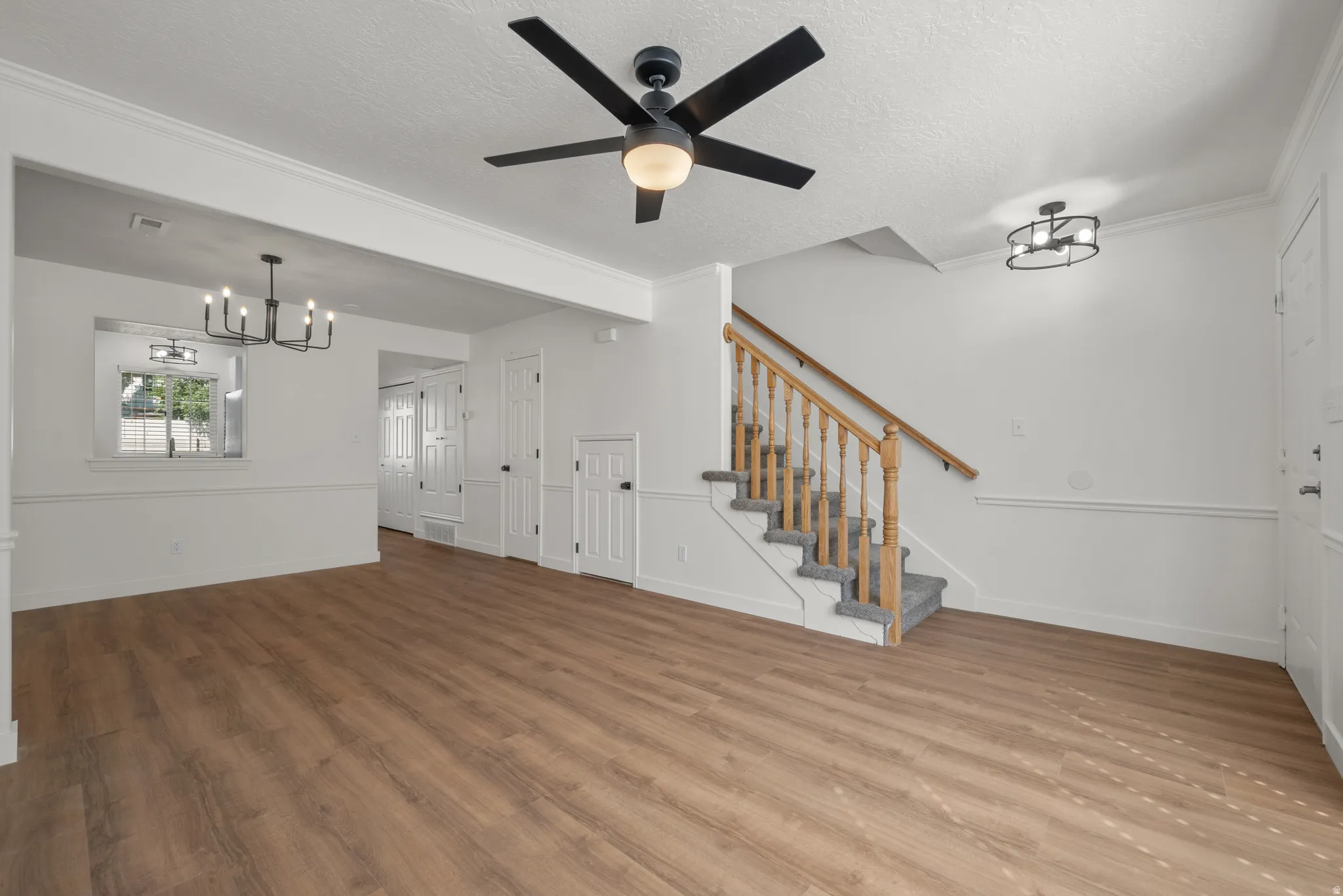 Spacious living area featuring wood-finish flooring, a contemporary ceiling fan, and a chandelier