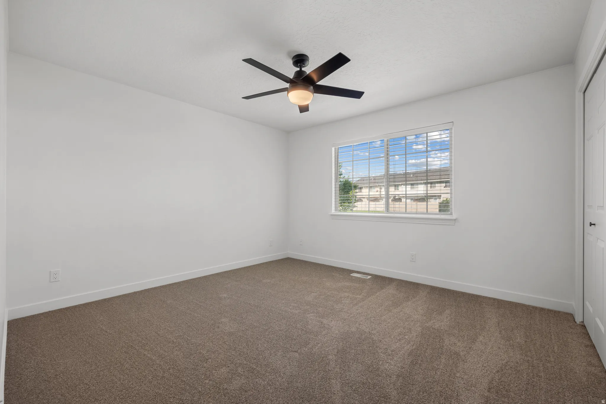 Neutral tone carpeted flooring, a ceiling fan with integrated lighting, a large window, and a white paneled door