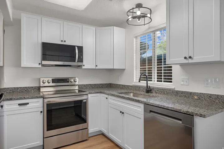 Kitchen featuring white cabinetry, stone-finish countertops, stainless steel appliances, and a window with blinds