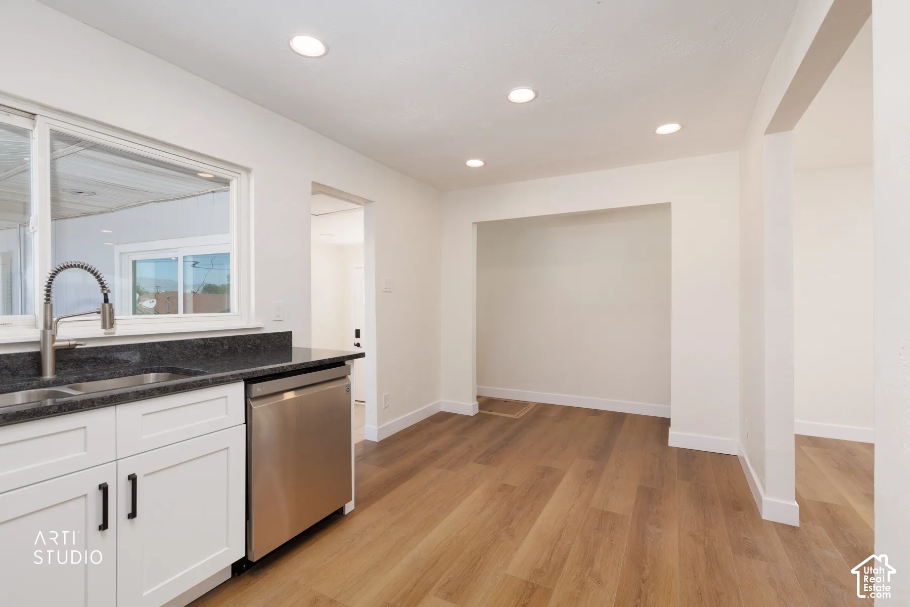 Kitchenette featuring recessed lighting, a stainless steel sink, a stainless steel dishwasher, white cabinetry with dark hardware, and wood-finish flooring