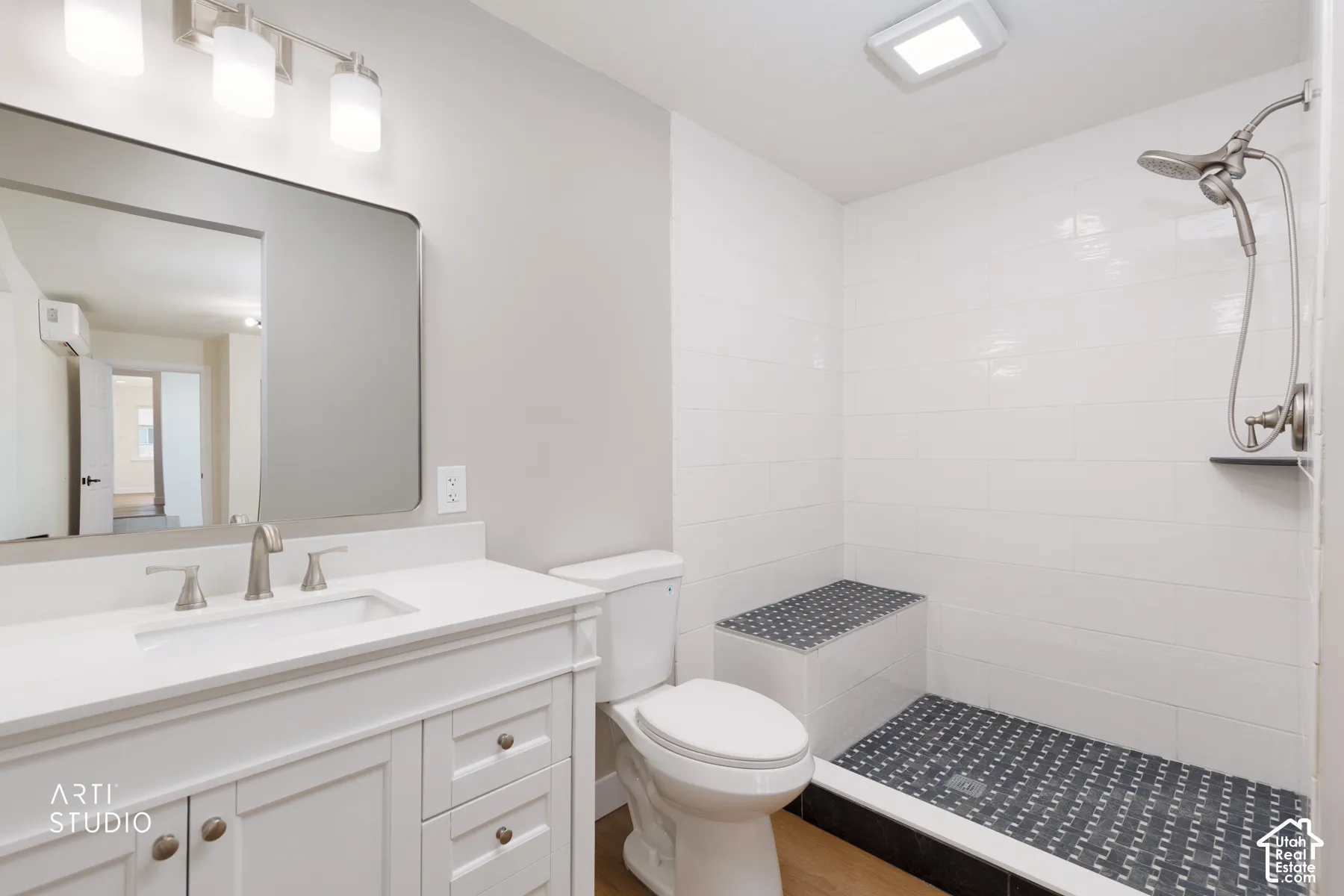 White vanity with an integrated sink and brushed nickel faucet, large wall mirror, walk-in shower with a built-in bench, and a dual-head shower system