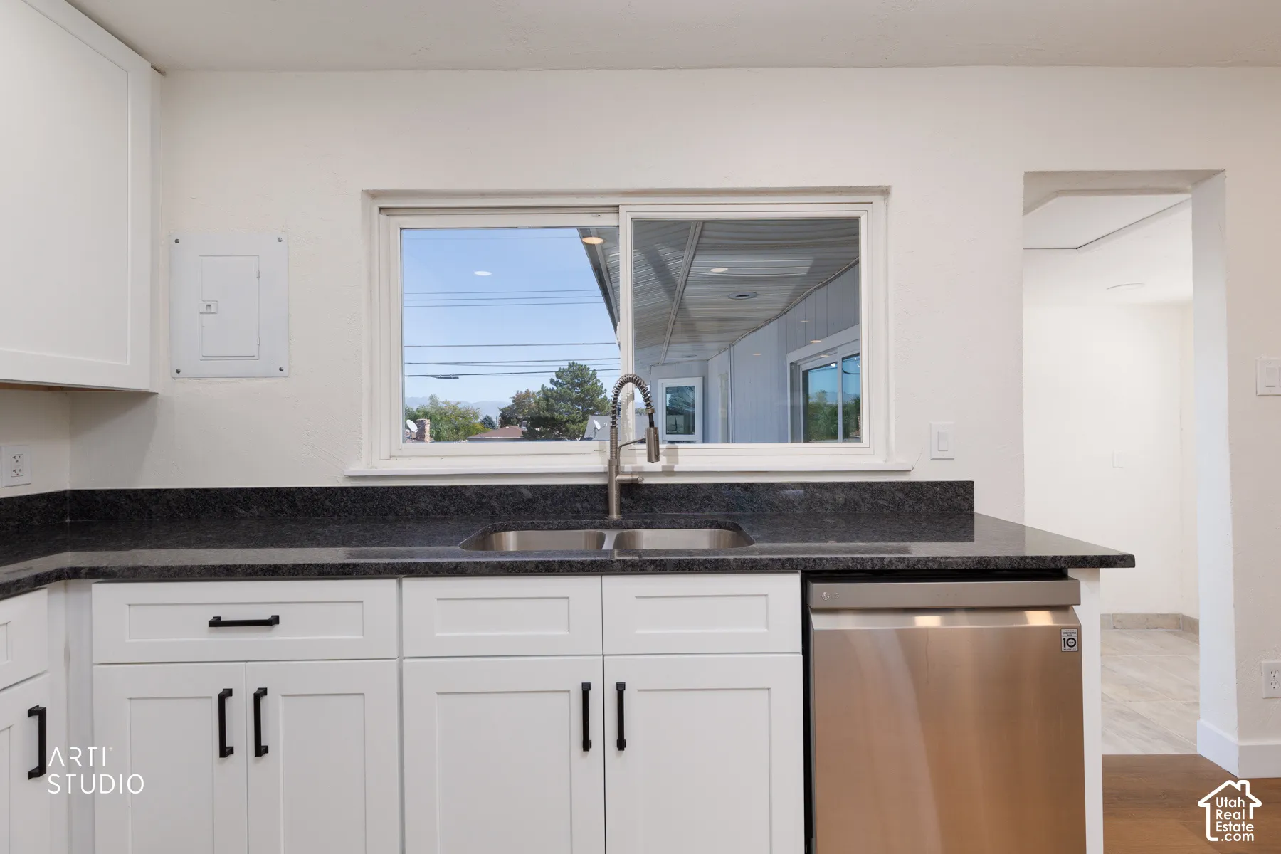 White cabinetry with black hardware, dark stone countertops, stainless steel sink, and stainless steel dishwasher