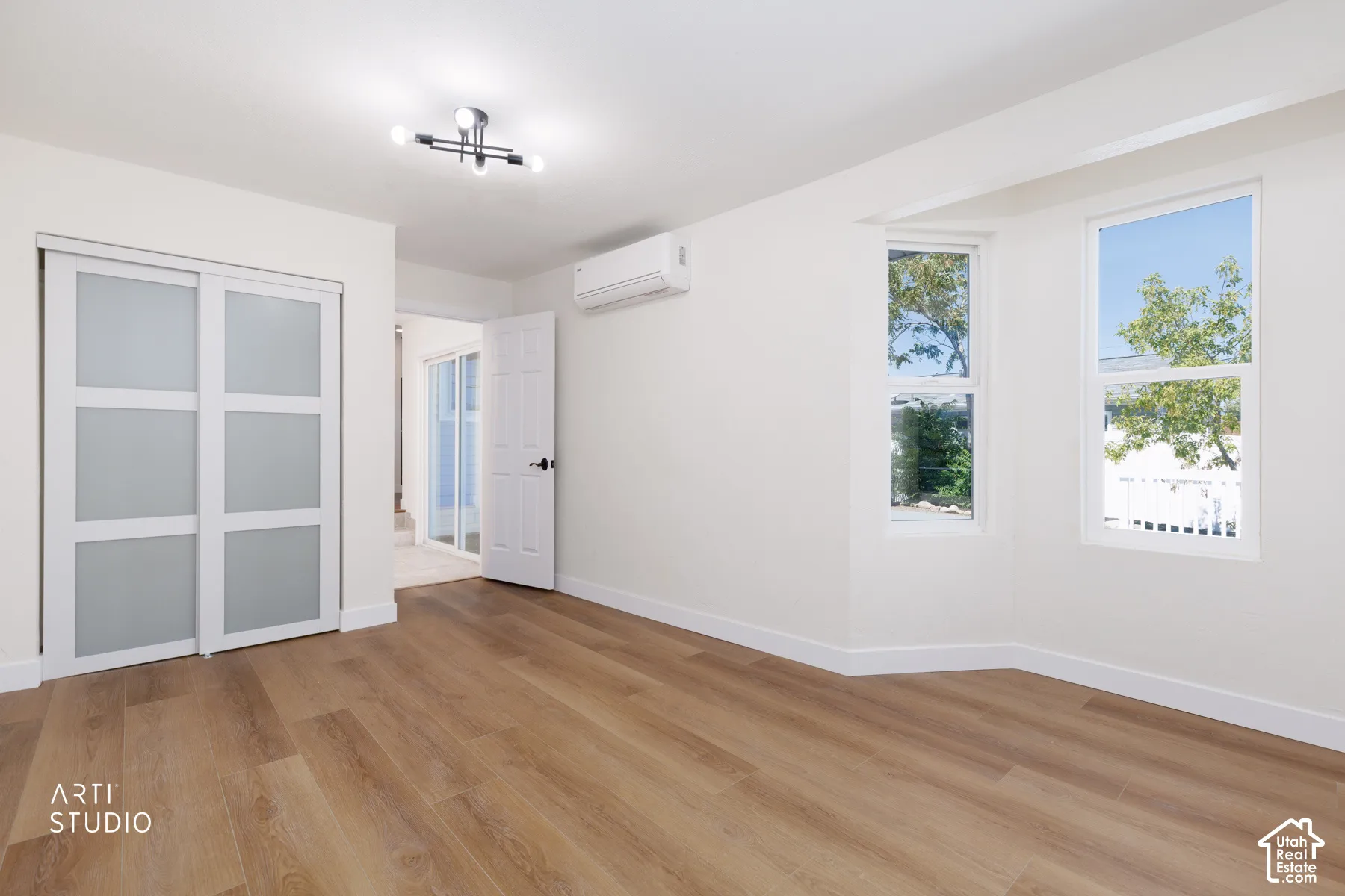 Wood-finish flooring throughout, white walls, modern ceiling light fixture, dual pane windows, and sliding closet doors with frosted panels
