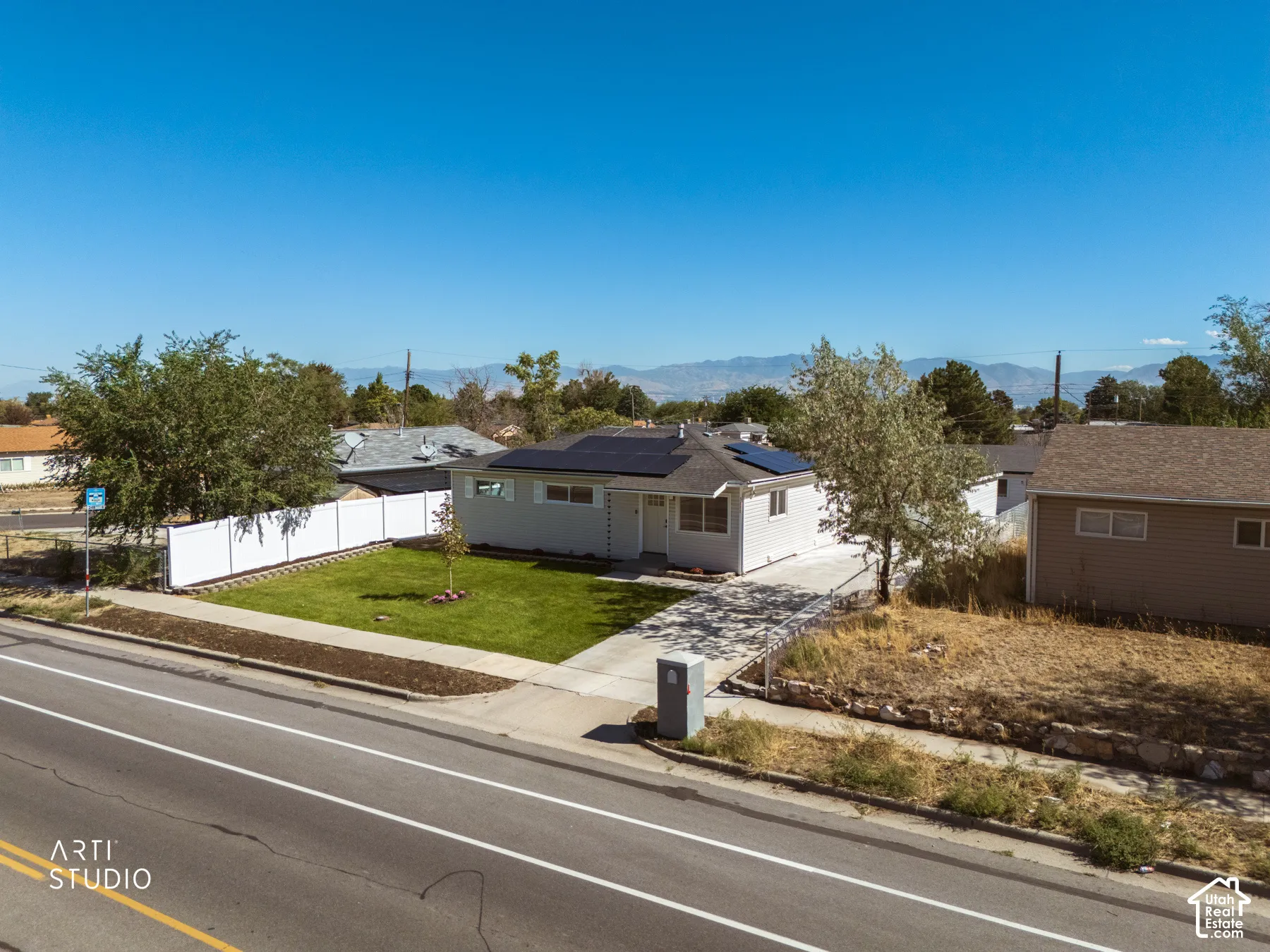 Single-story residence featuring a paved driveway, a manicured lawn, solar panels, and a white privacy fence