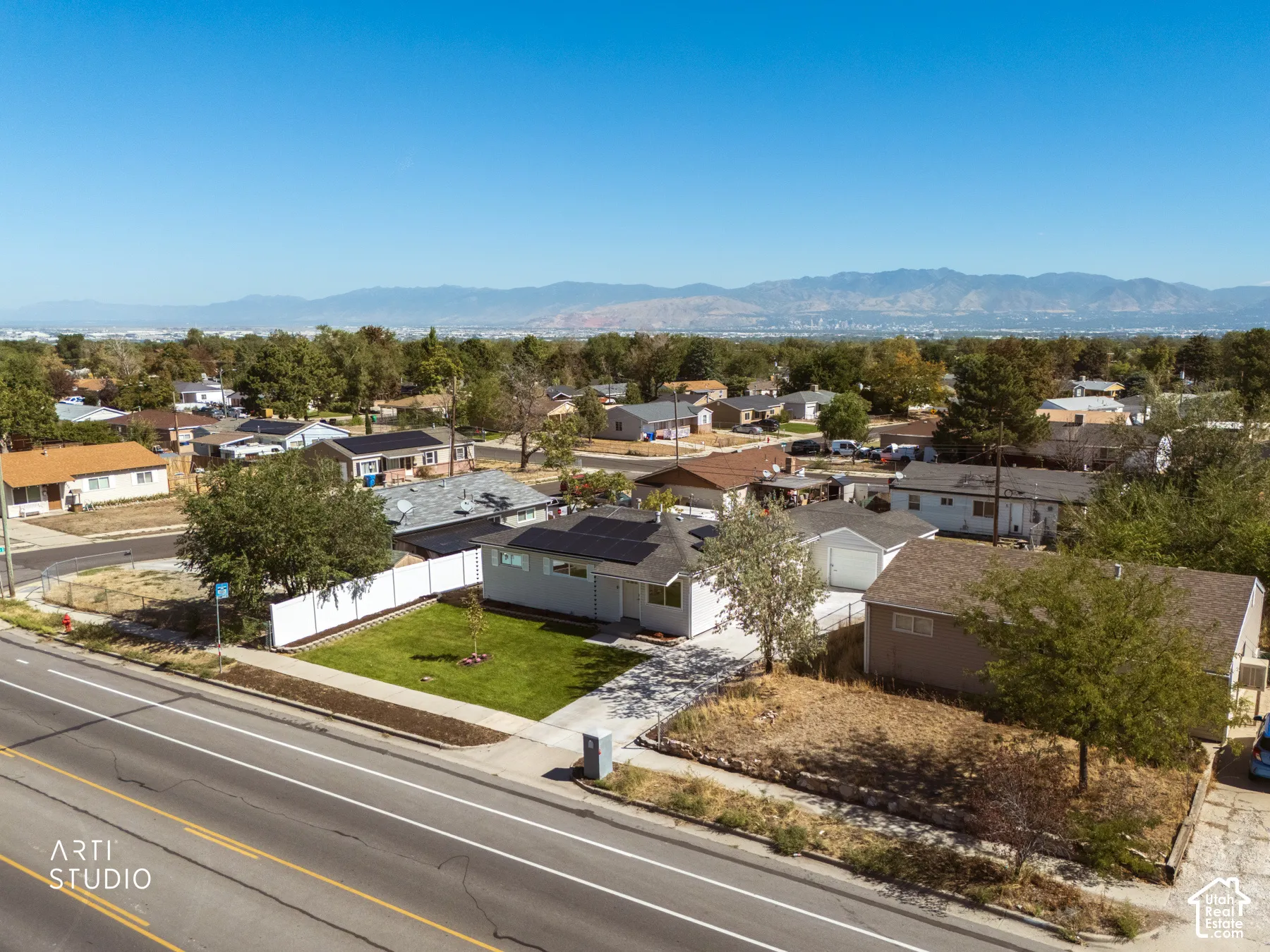 Manicured front lawn, white privacy fence, solar panels, paved driveway, surrounding neighborhood