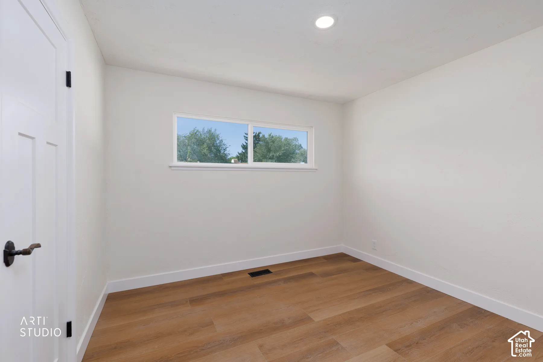 Recessed ceiling lighting, wood-finish flooring, white trim, white wall finishes, and a multi-pane window