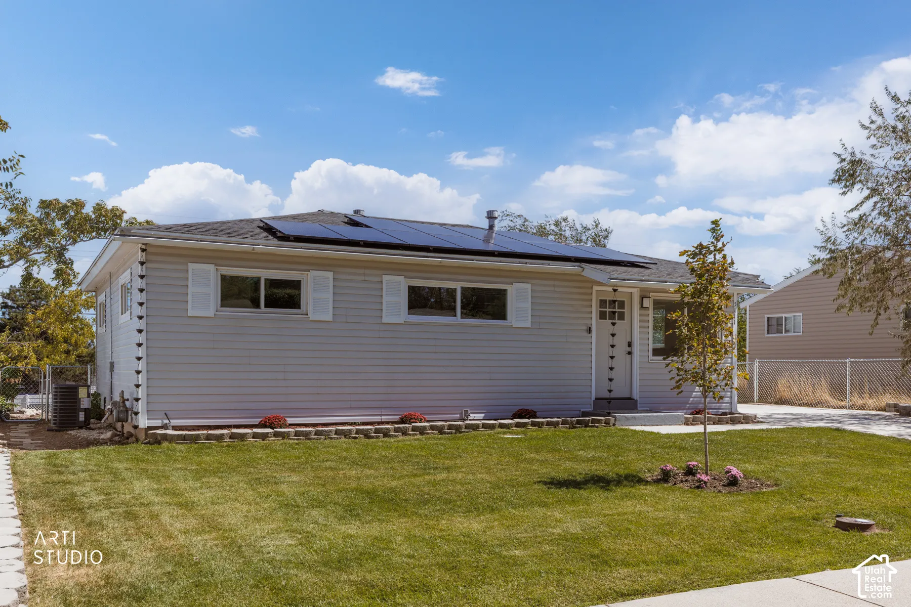 Gray siding exterior with white window shutters, a front entry door with glass panels, and rooftop solar panels