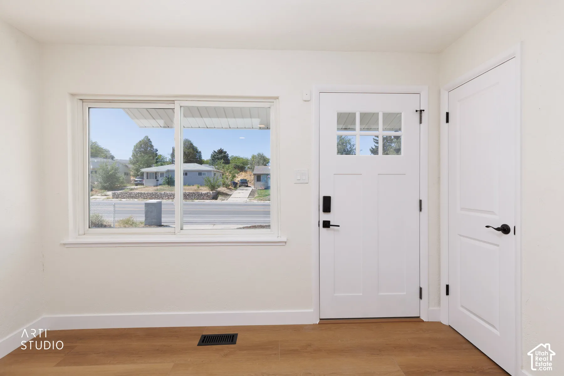 Wood-finish flooring, white walls, white trim, white paneled door with matte black hardware, and an additional white door with matte black hardware