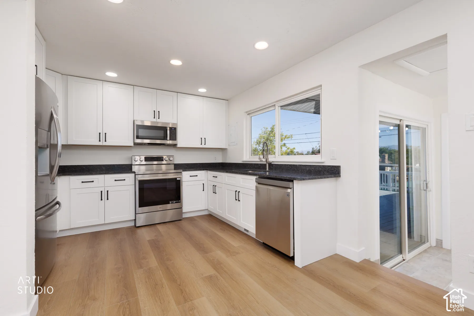 White cabinetry, dark stone countertops, stainless steel appliances, wood-finish flooring, and recessed lighting