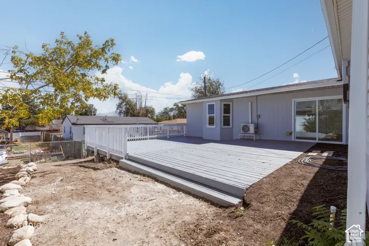 Expansive wood-finish deck with white railing, featuring multiple steps, a sliding glass door, and exterior siding