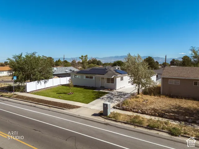 Single-story residence featuring a paved driveway, a manicured lawn, solar panels, and a white privacy fence