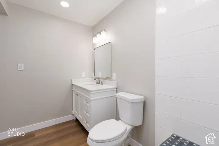 White vanity with a single basin, recessed lighting, wood-finish flooring, and white rectangular wall tiling