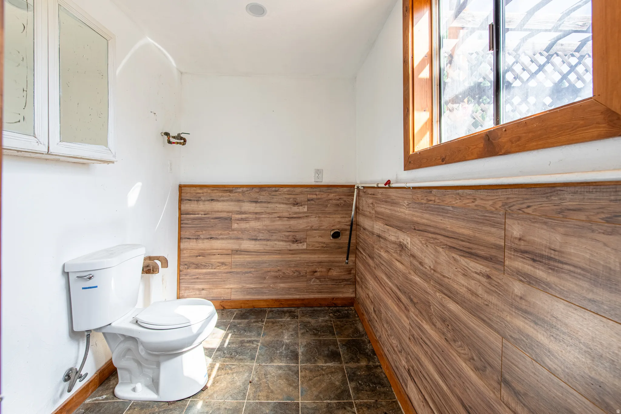 White ceramic toilet, wood-finish wall paneling, and a wood-framed window