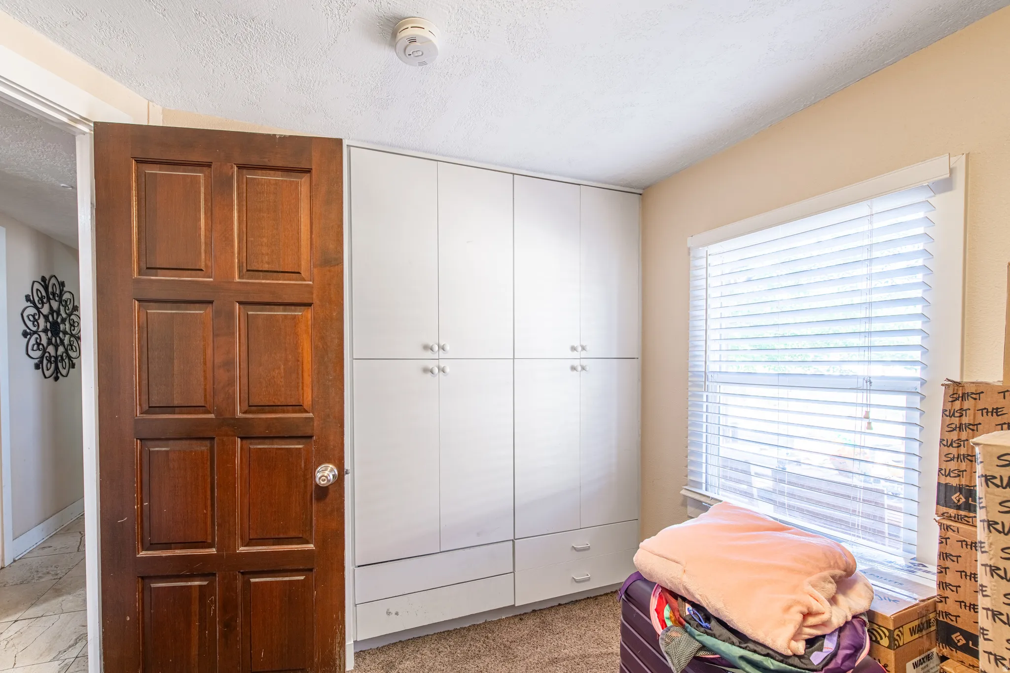 Built-in white cabinetry with chrome hardware, an egress window with blinds, and paneled wood door