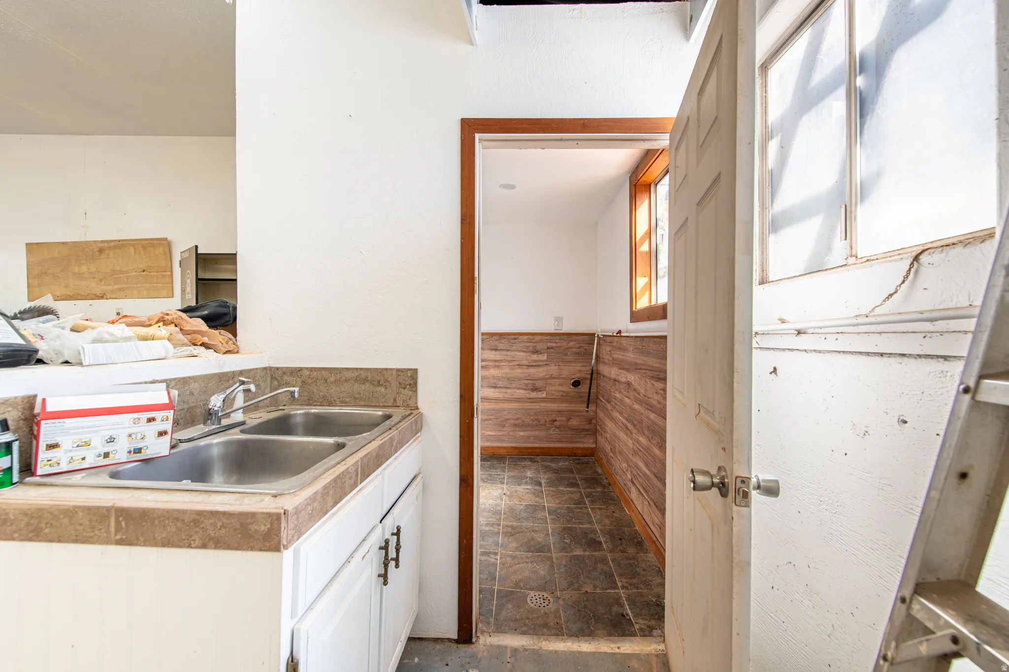 Sink cabinet with a dual basin stainless steel sink, tile countertop, and white cabinetry