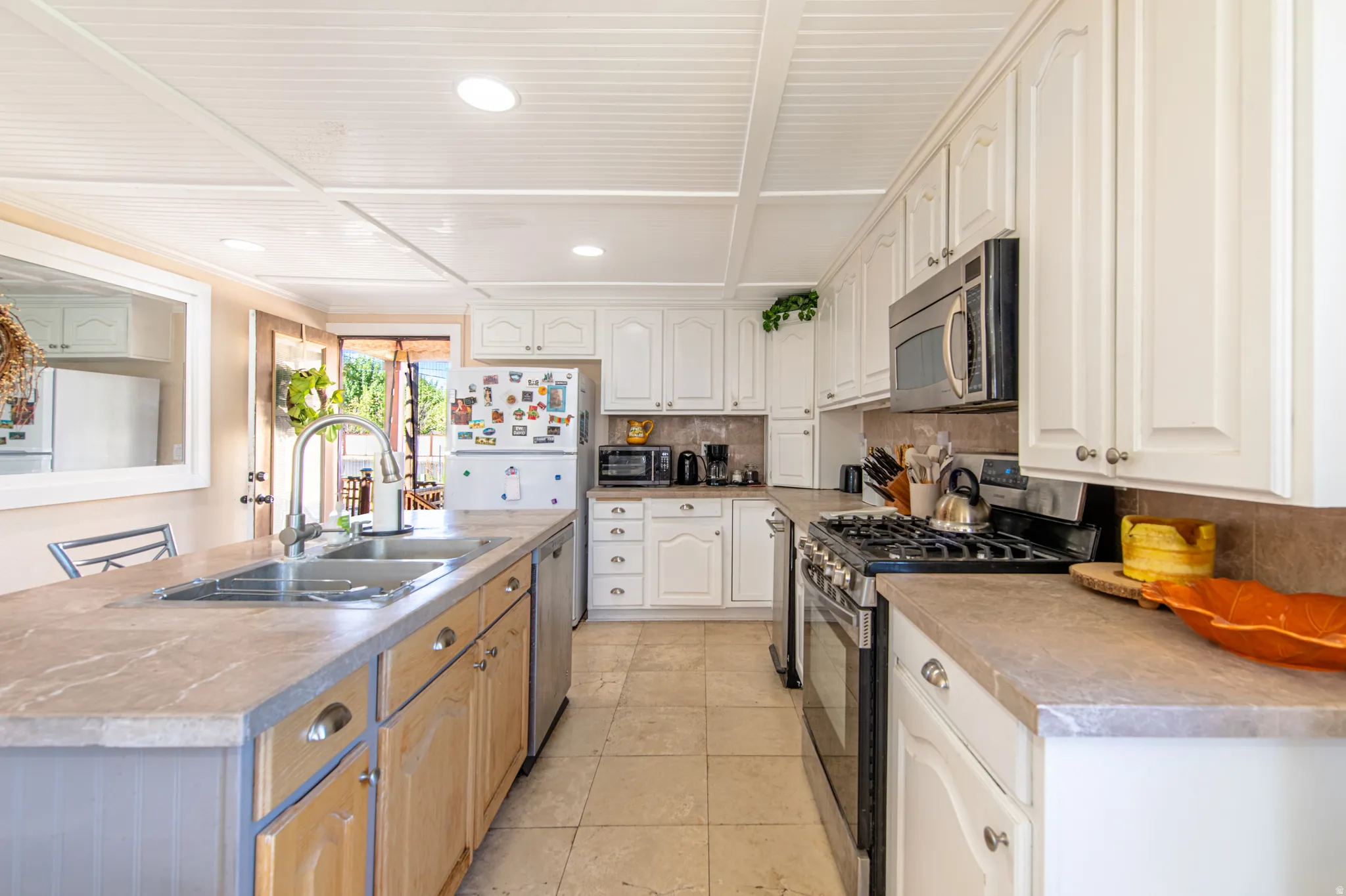 White cabinetry, stainless steel appliances, dual basin sink with gooseneck faucet, light-toned countertops, and tile flooring
