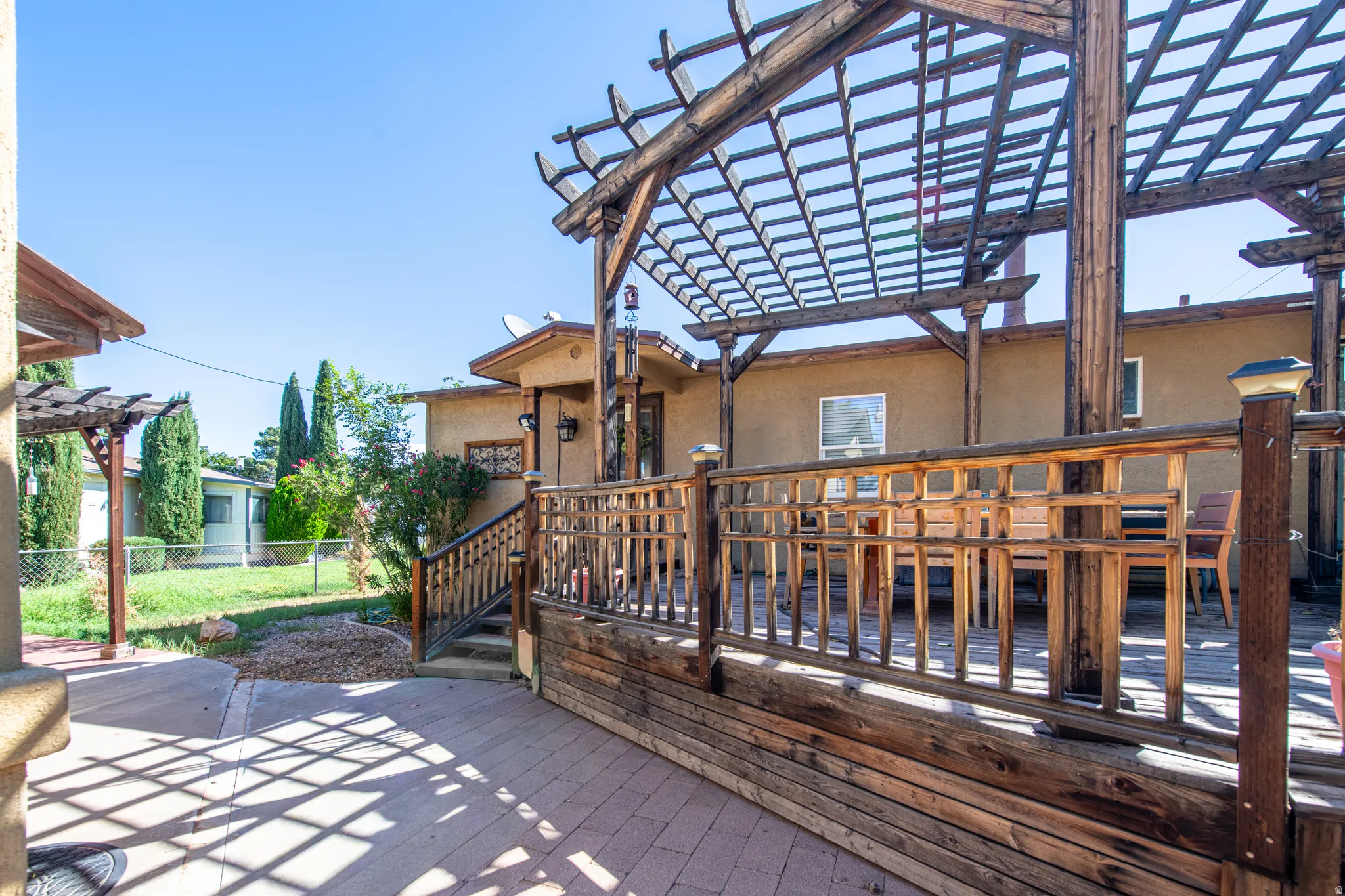 Expansive outdoor patio featuring a wood deck, pergola, and brick-patterned hardscaping
