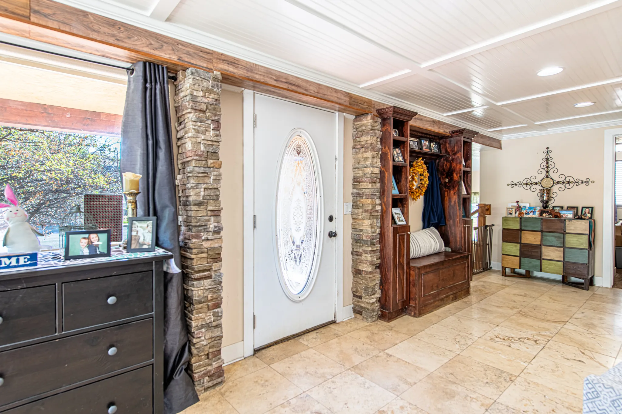 Entryway featuring stone veneer accents, an oval decorative glass door, a built-in wood-finish hall tree, and large format tile flooring