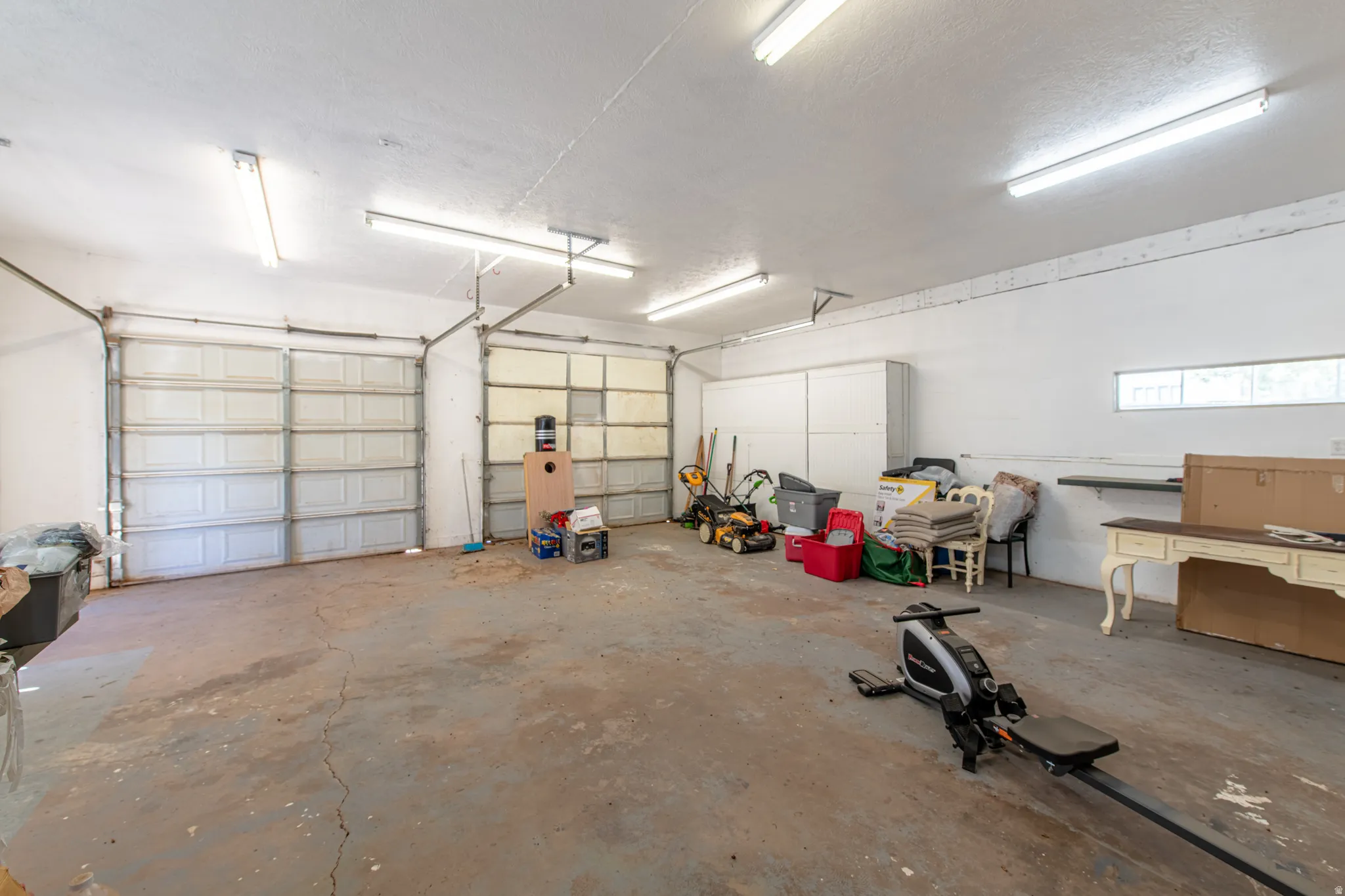 Spacious garage featuring two overhead doors, concrete flooring, overhead fluorescent lighting, and white walls