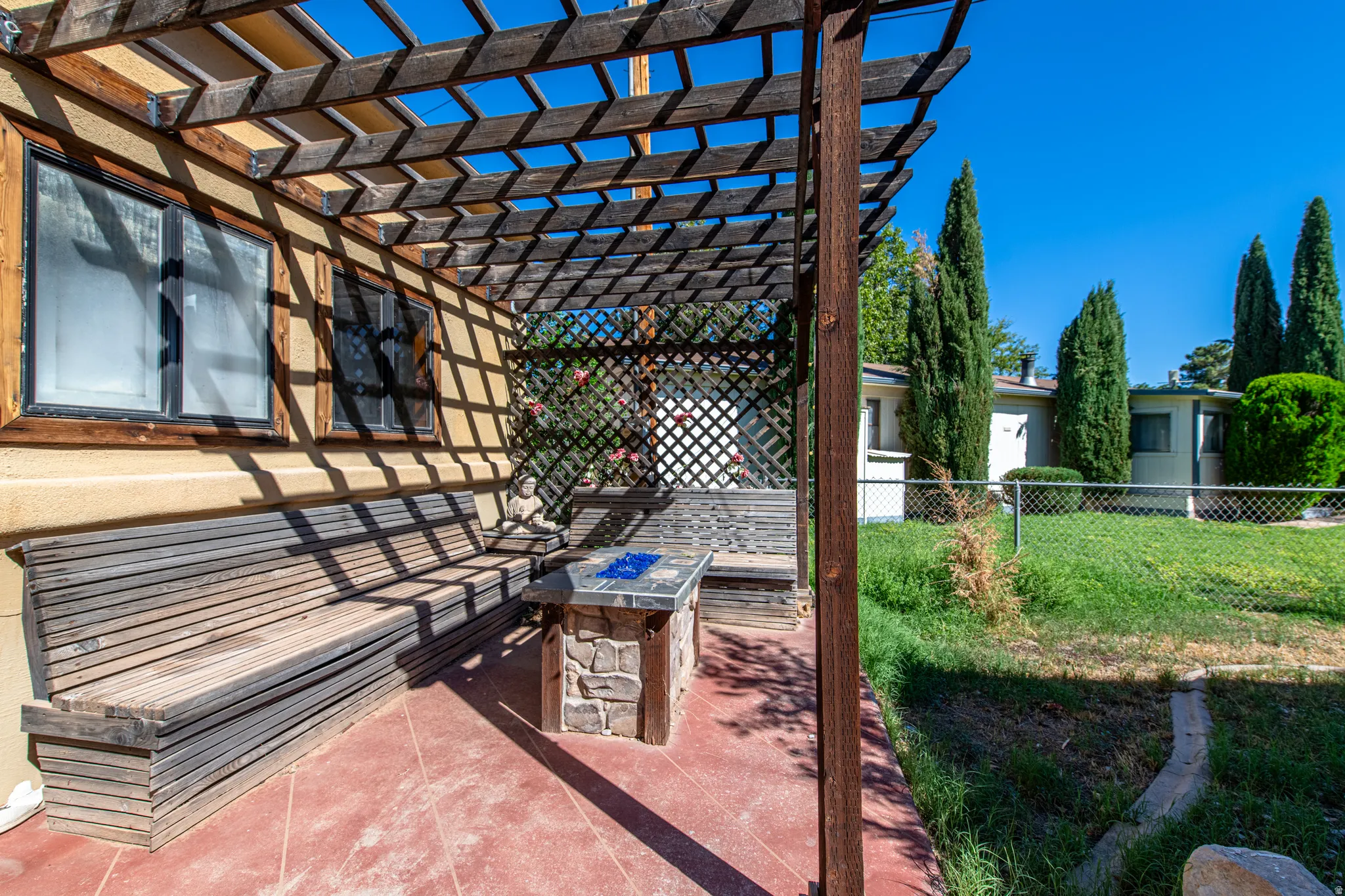 Attached wooden pergola with lattice detailing, built-in wooden bench seating, and an integrated stone-finish table