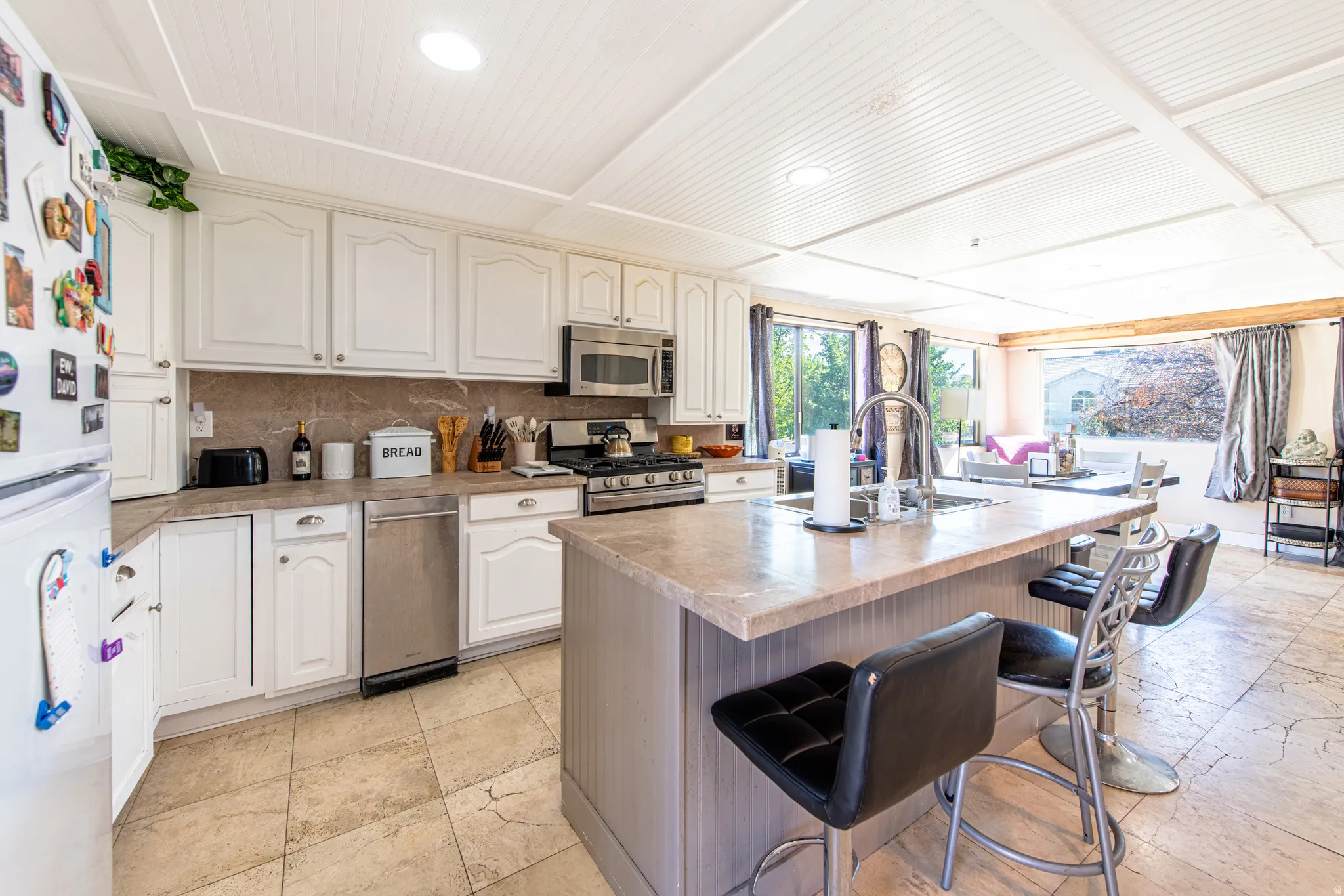 Kitchen featuring white cabinetry, stainless steel appliances, a center island with sink, and tile flooring