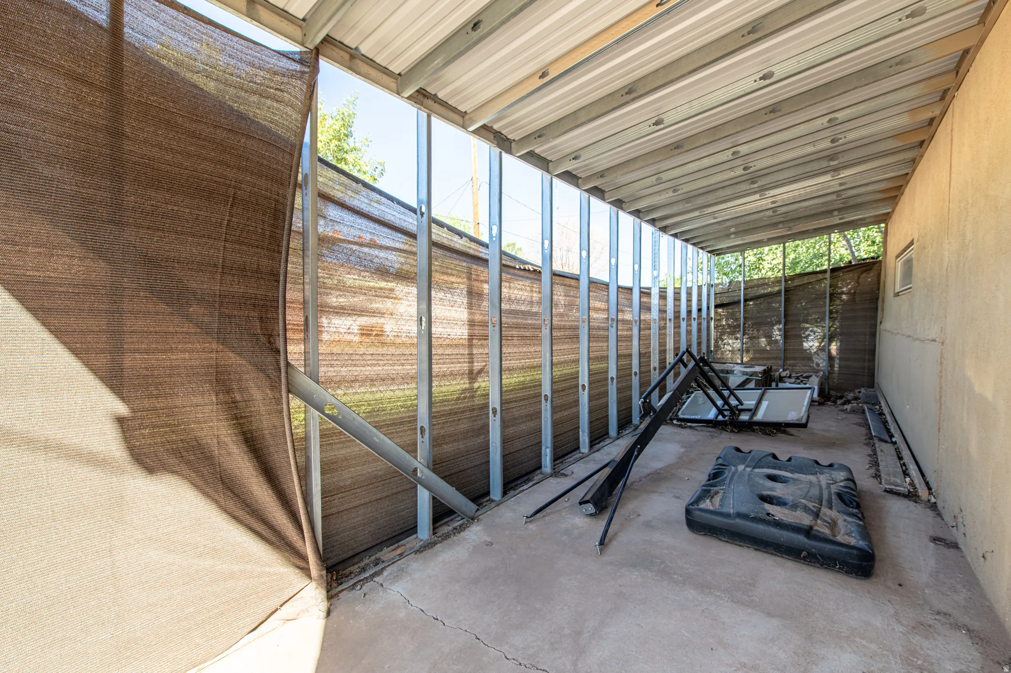 Concrete patio with corrugated metal roofing, supported by metal framing, and a partial privacy screen