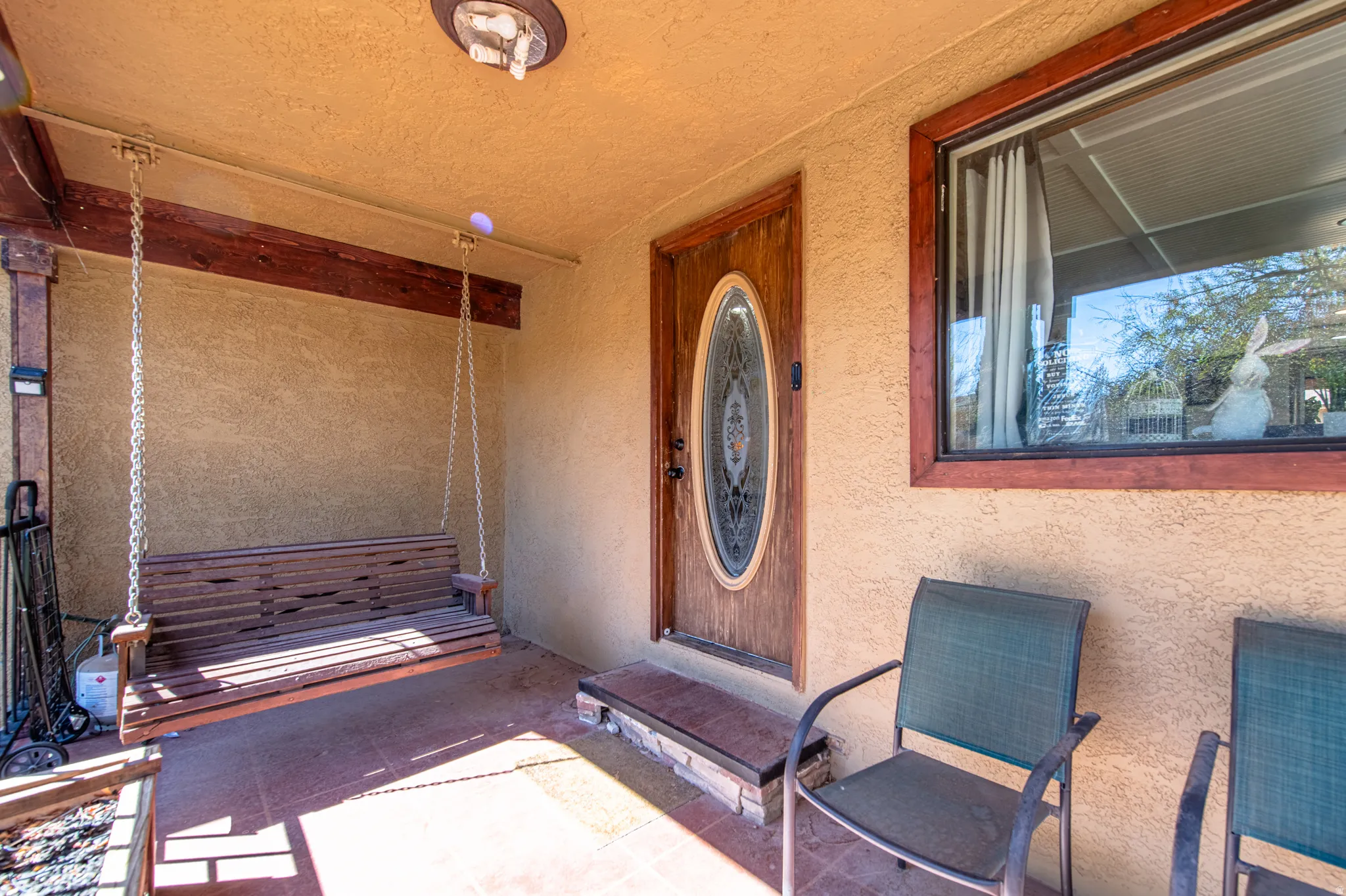 Covered front porch featuring a wood-panel swing, oval-insert front door, and a single-pane window with wood trim