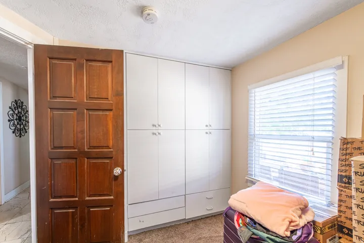 Built-in white cabinetry with chrome hardware, an egress window with blinds, and paneled wood door