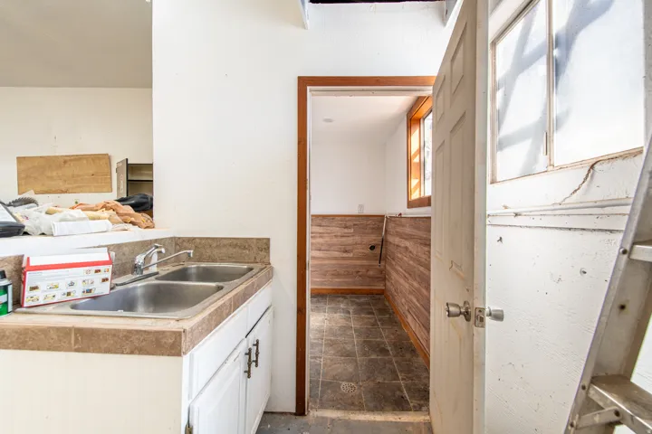 Sink cabinet with a dual basin stainless steel sink, tile countertop, and white cabinetry